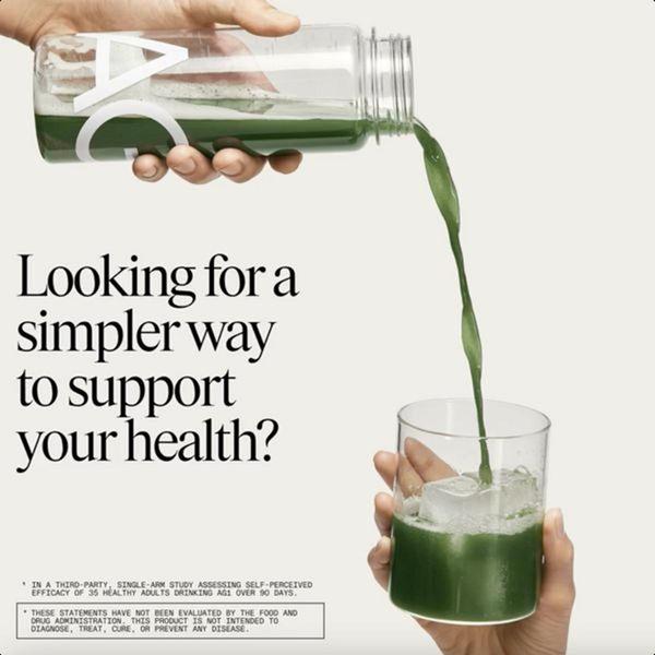 A clean, high-contrast shot of a greens powder drink being poured into an ice-filled glass, centered on a neutral background.